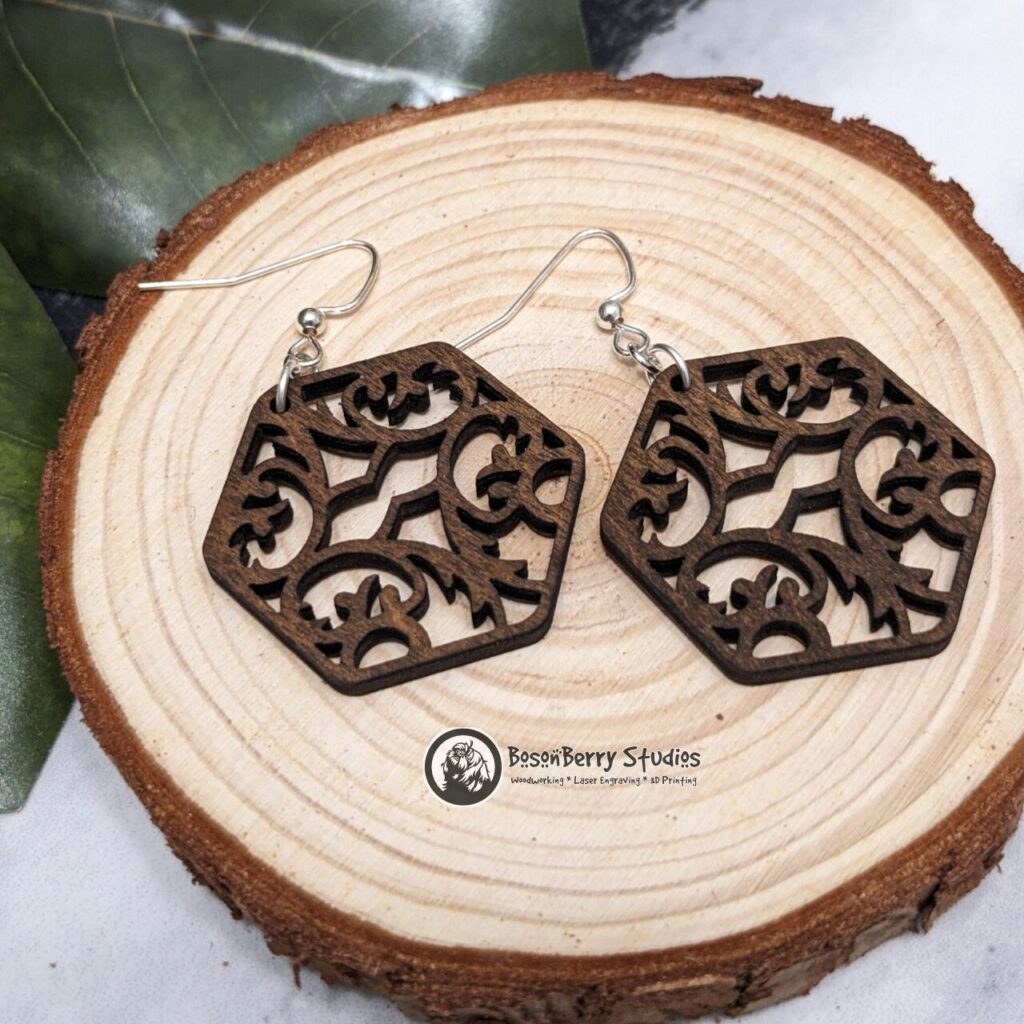 Damask Cutout Wooden Earrings, hexagon shaped, brown stained, posed on a slice of wood with magnolia leaves accent.