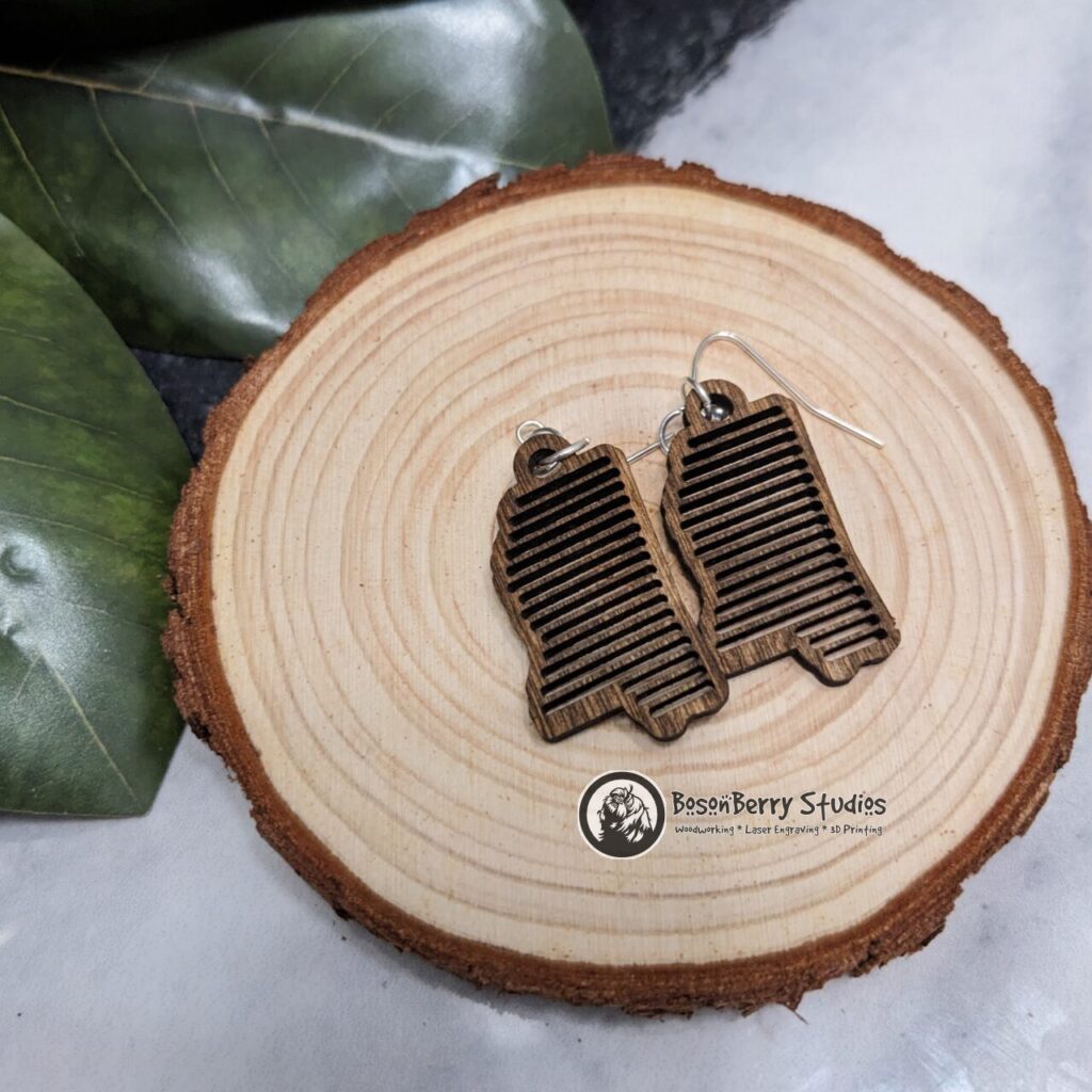 Wooden "State Line Collection" Earrings, Mississippi Outlines with decorative variegated cutouts, displayed on a slice of wood with magnolia leaves in background.