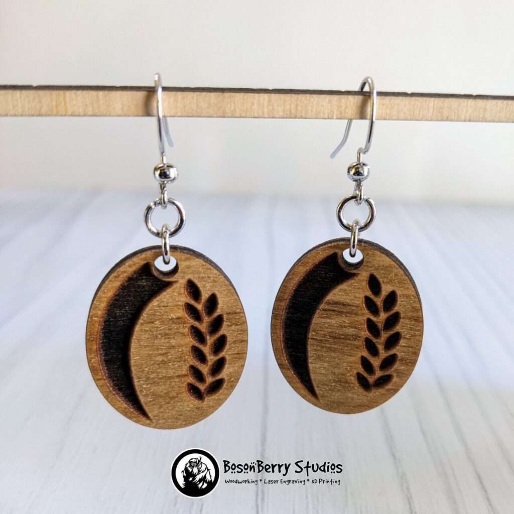 Wooden vertical Sourdough loaf earrings with laurel pattern, hanging from a wooden dowel in front of a white backdrop.