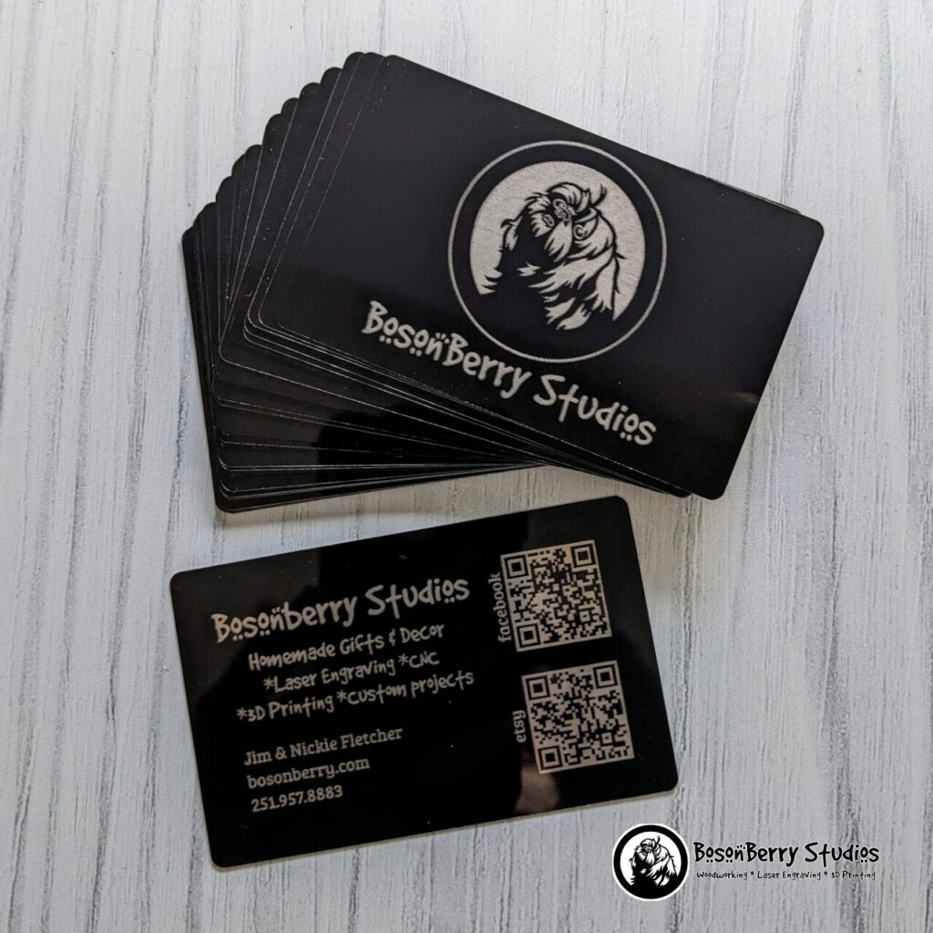 Black aluminum business cards, engraved with BosonBerry Studios information, displayed in a stack on a white wood backdrop.