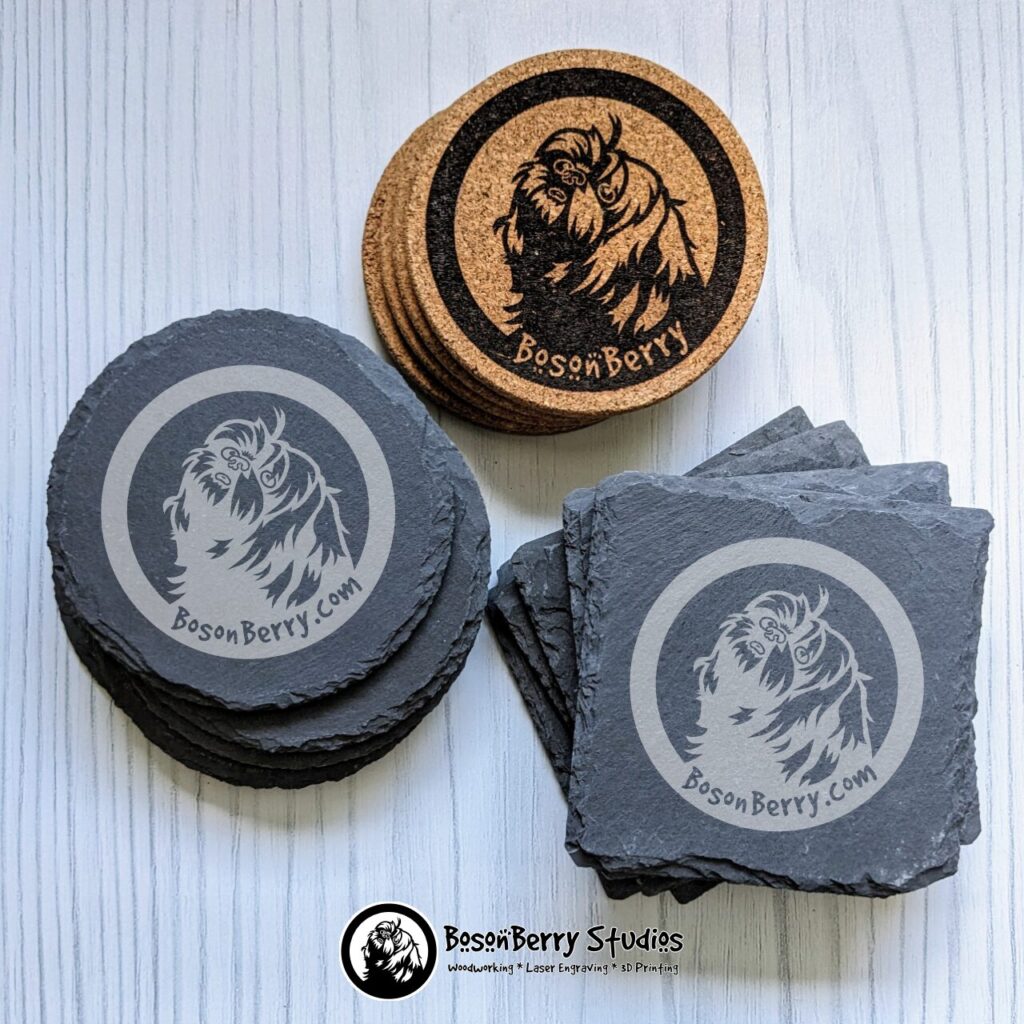 3 stacks of different types of coasters, round cork, round slate, and square slate, engraved with the round BosonBerry Studios logo, on a white wood backdrop.