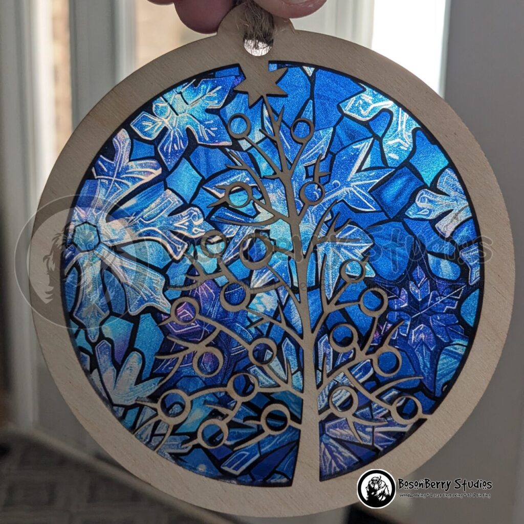 Deco Christmas Tree round layered ornament. Top layer is natural wood border with a center cutout revealing a skeletal Christmas tree with circular ornaments. Backer is thin blue acrylic with a snowflake stained glass pattern. Made by BosonBerry Studios.
