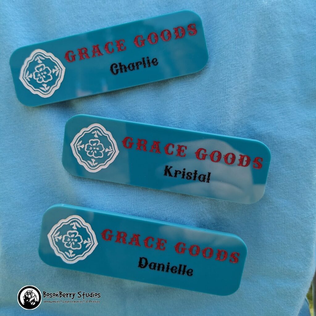 Three rectangular nametags made of paint-filled turquoise acrylic on a teal fabric background.