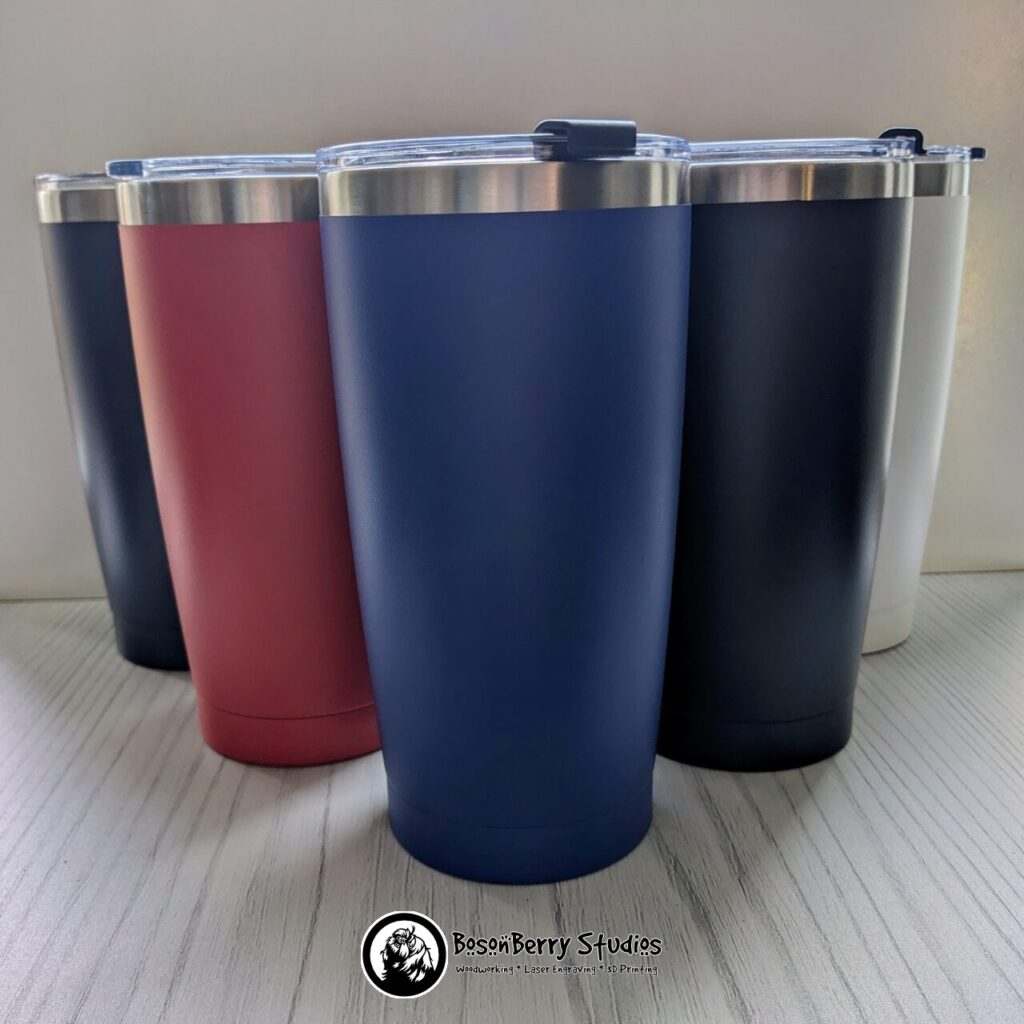 A group of five 20oz powder-coated aluminum tumblers, in navy, red, blue, black and white, on a white wood floor with a white backdrop. Photo by BosonBerry Studios.