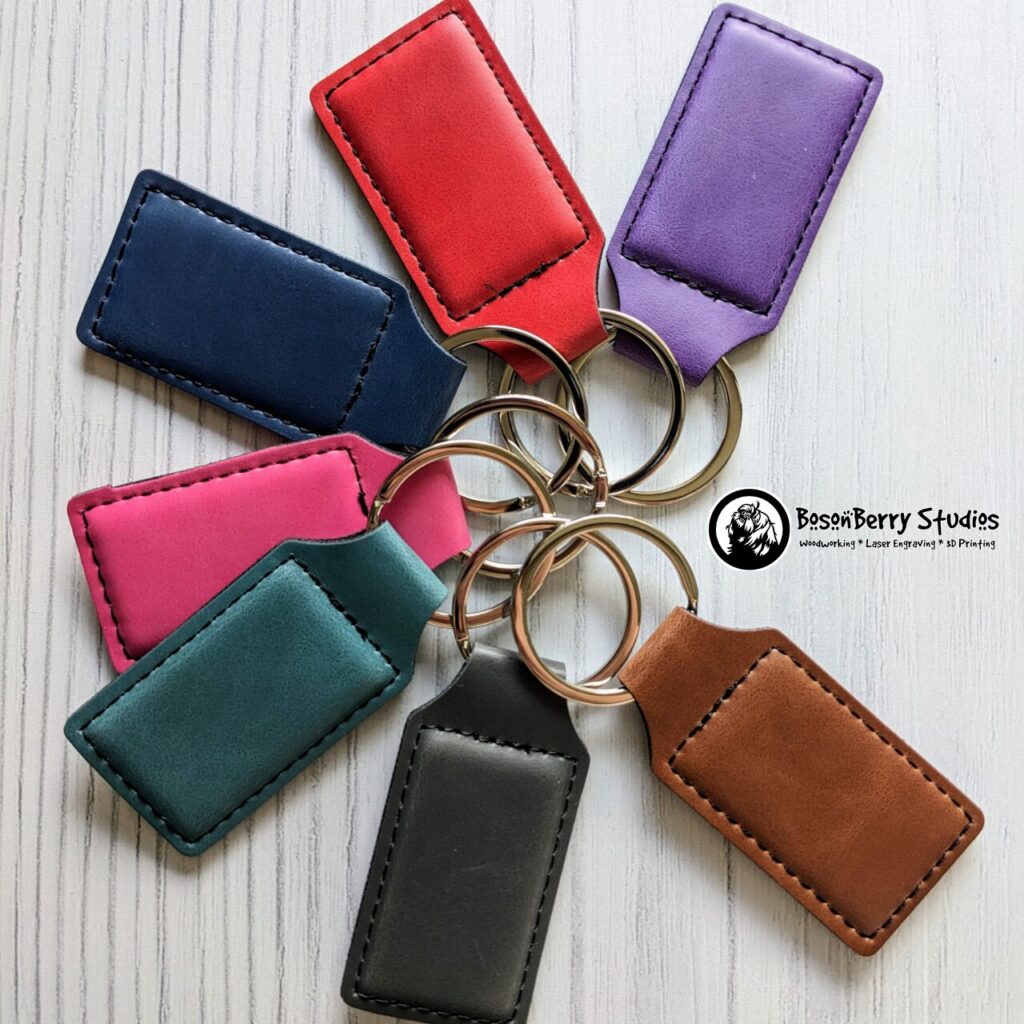 Display of seven leatherette keychains fanned out of a white wood backdrop. Colors are purple, red, blue, pink, teal, grey and brown. Photo by BosonBerry Studios.